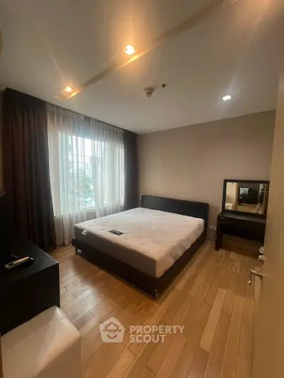 Spacious bedroom with large window and modern furnishings in a stylish apartment.