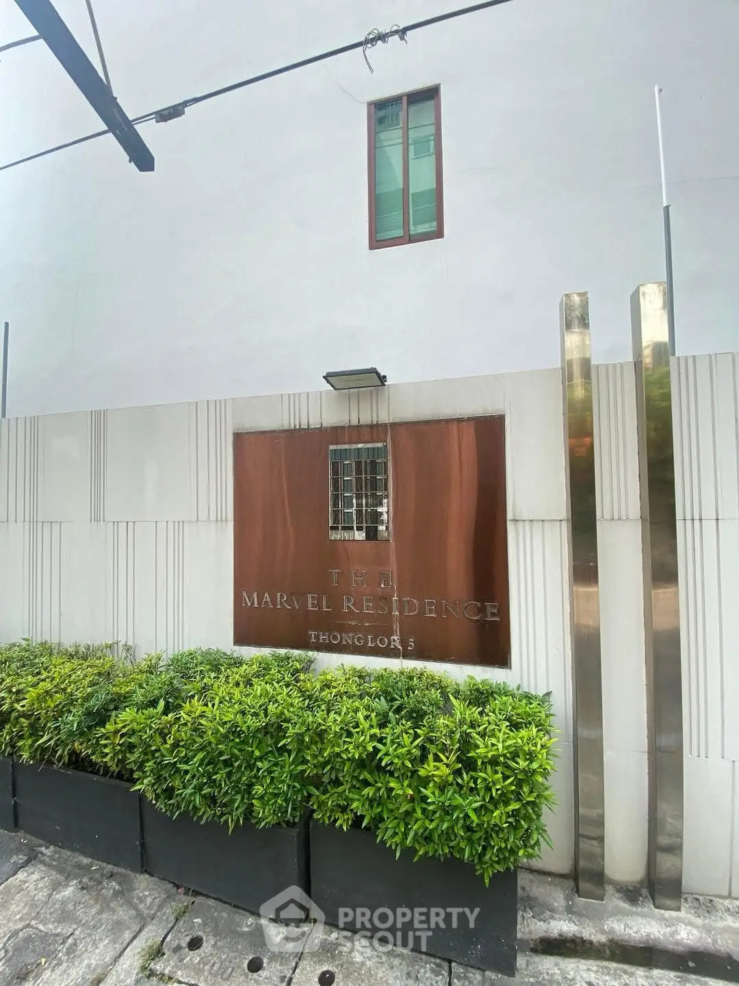 Modern building entrance with sleek design and lush greenery at Ten Marvel Residence.