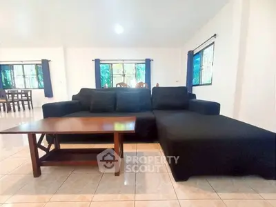 Spacious living room with modern black sofa and wooden coffee table, bright windows, and tiled flooring.