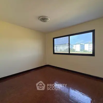 Spacious empty room with large window and wooden flooring, offering potential for customization.