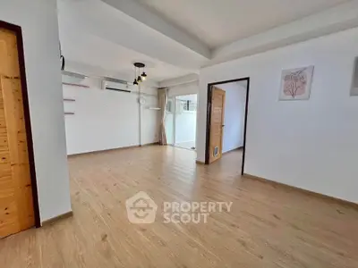 Spacious open-plan living room with wooden flooring and modern lighting in a bright apartment.