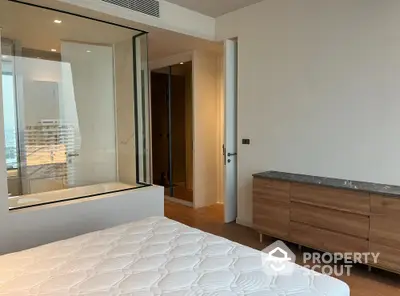 Modern bedroom with glass partition and city view, featuring wooden dresser and cozy ambiance.