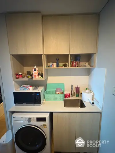 Compact laundry area with washer, sink, and storage cabinets in modern apartment.