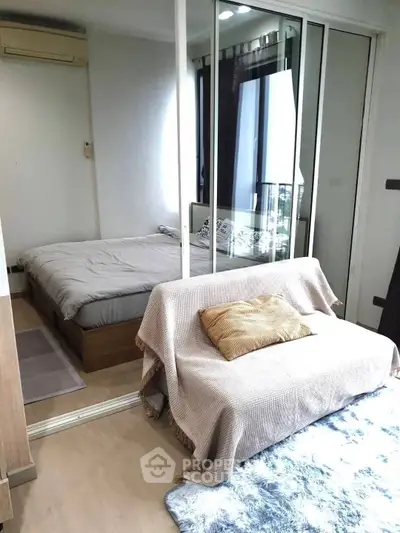 Cozy bedroom with mirrored closet and small sofa, perfect for urban living.