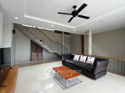 Modern living room with sleek design, featuring a black leather sofa, ceiling fan, and stylish staircase.
