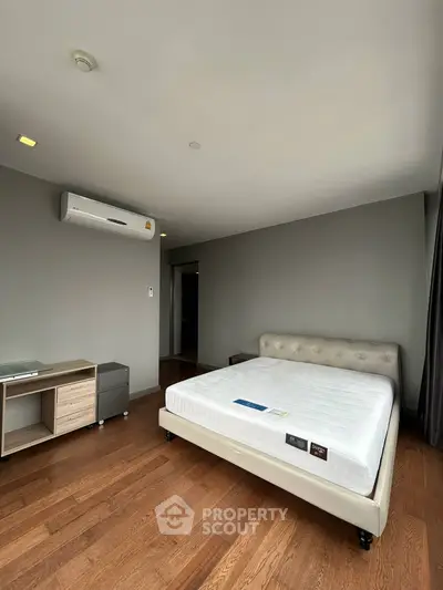 Spacious bedroom with modern design and hardwood floors, featuring a comfortable bed and air conditioning.