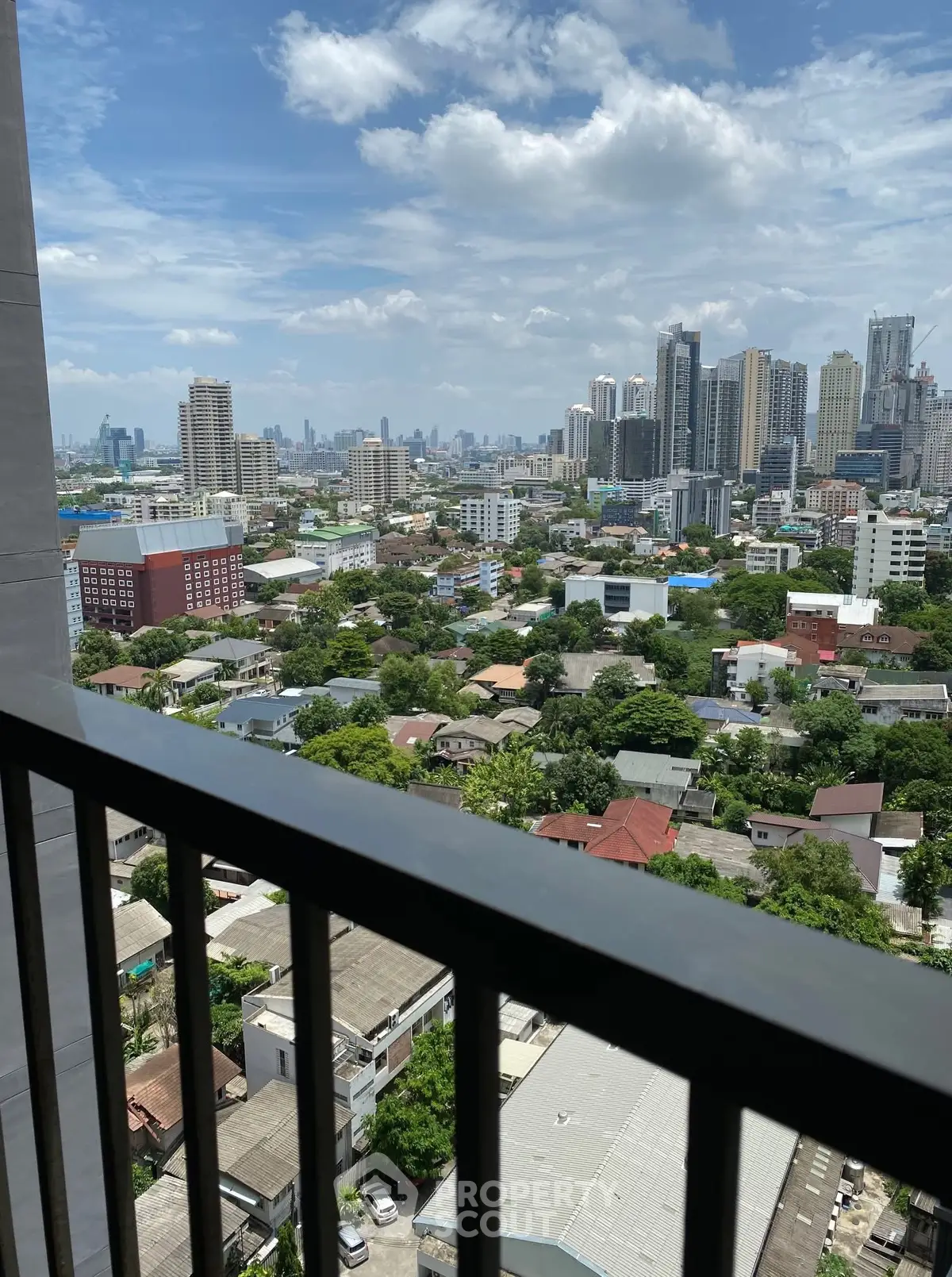 Stunning cityscape view from a high-rise balcony overlooking urban skyline and lush greenery.
