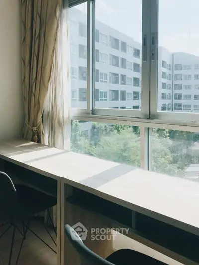 Bright study area with large window offering a view of modern apartment buildings.