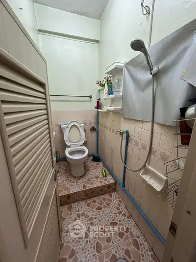 Compact bathroom with shower and toilet, featuring tiled floor and wall storage.