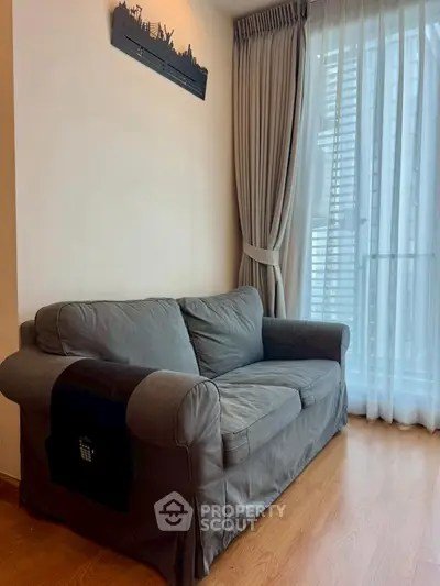 Cozy living room with a grey sofa and large window with curtains.