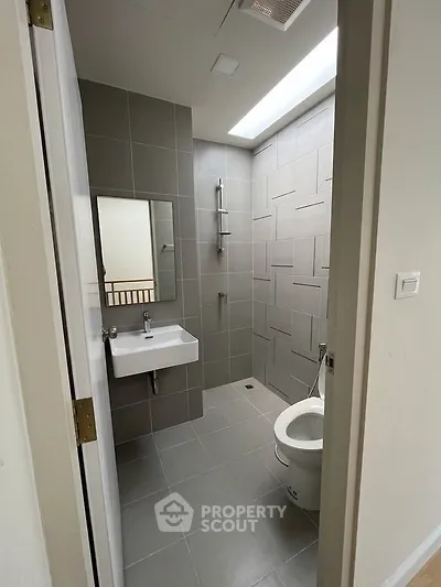 Modern bathroom with sleek gray tiles and skylight, featuring a wall-mounted sink and shower area.