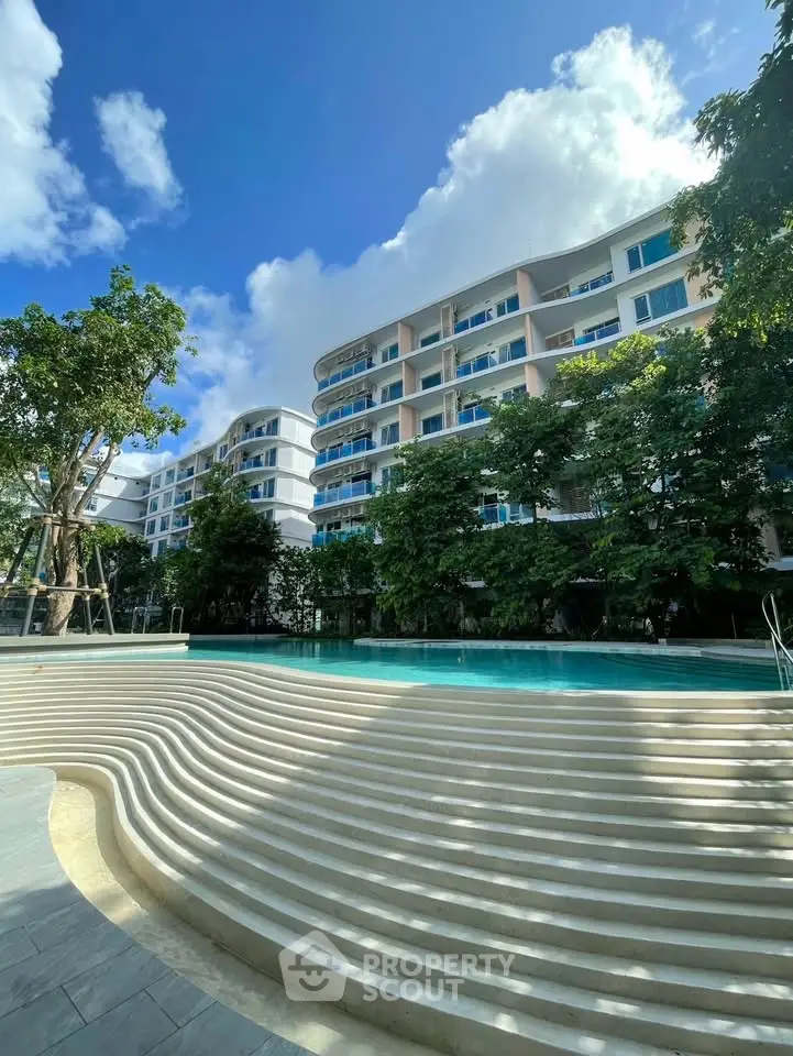 Luxurious modern apartment complex with stunning pool and lush greenery under a clear blue sky.