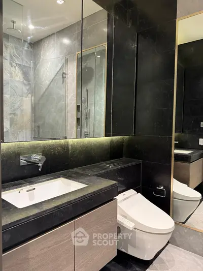 Luxurious modern bathroom with sleek black and gray tiles, featuring a stylish sink and toilet.