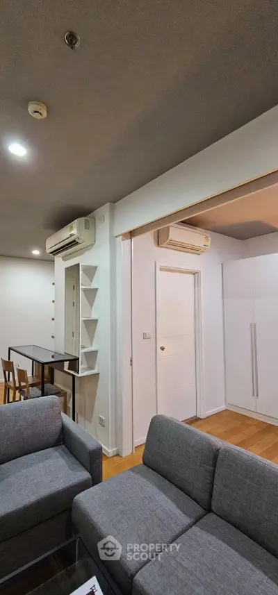 Modern living room with sleek gray sofas and air conditioning, featuring open layout and stylish shelving.