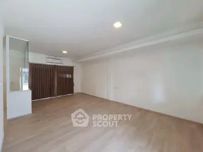 Spacious empty living room with wooden flooring and large window, perfect for customization.