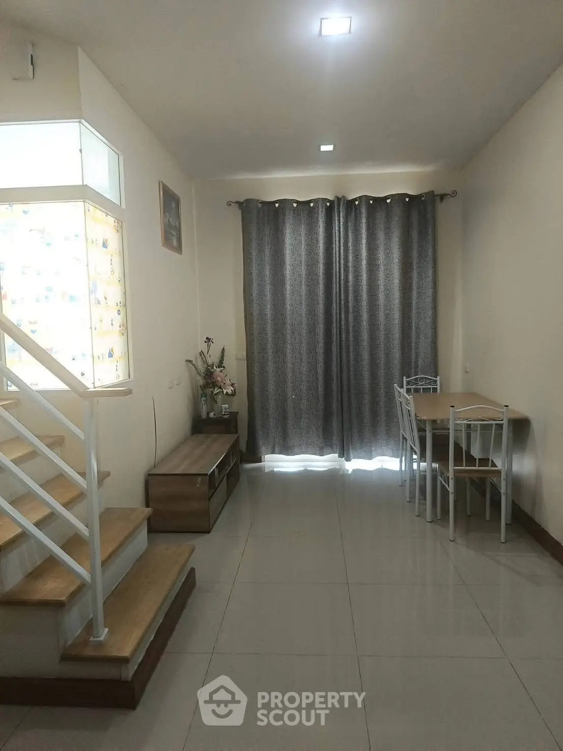 Spacious living room with modern staircase and dining area, featuring elegant curtains and natural light.