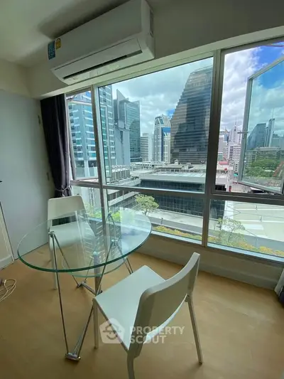 Modern apartment with city view, featuring glass table and chairs near large window.