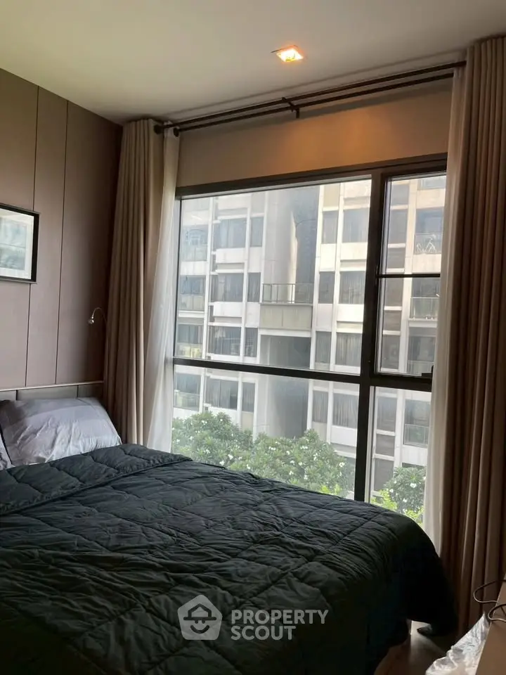 Cozy bedroom with large window offering urban view in modern apartment.