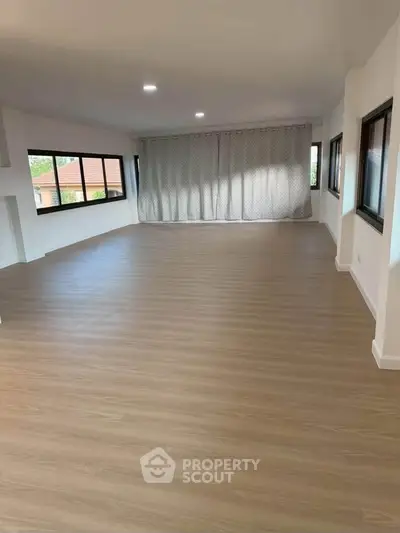 Spacious empty room with large windows and wooden flooring, ideal for customization.