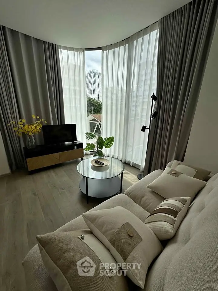 Modern living room with floor-to-ceiling windows and cozy beige sofa, offering a stunning city view.