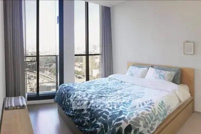 Spacious bedroom with large windows offering stunning city views, modern decor, and ample natural light.