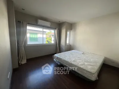 Spacious bedroom with large window and air conditioning, featuring a comfortable mattress on wooden flooring.