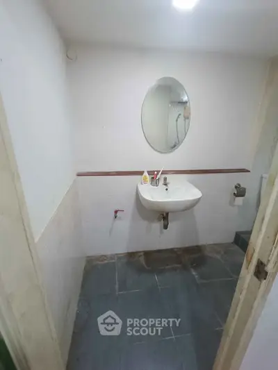 Compact bathroom with wall-mounted sink and oval mirror