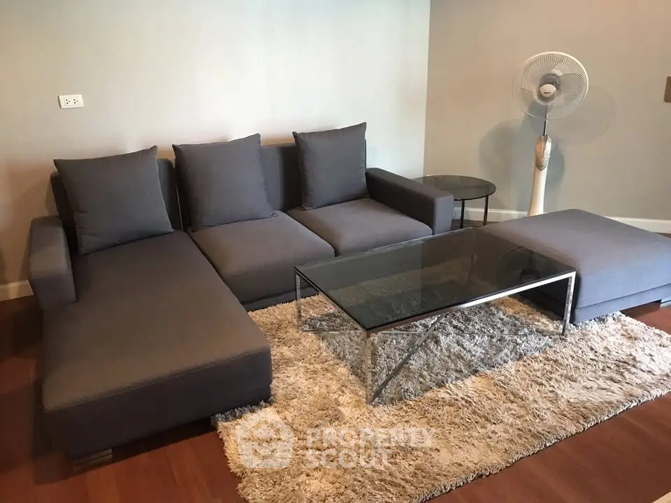 Modern living room with stylish gray sofa and glass coffee table on plush rug