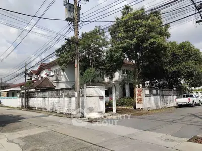 Charming corner house with lush trees and white walls in a serene neighborhood.