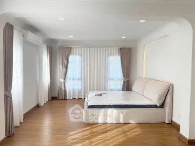 Spacious bedroom with elegant curtains and natural light, featuring a comfortable bed and wooden flooring.