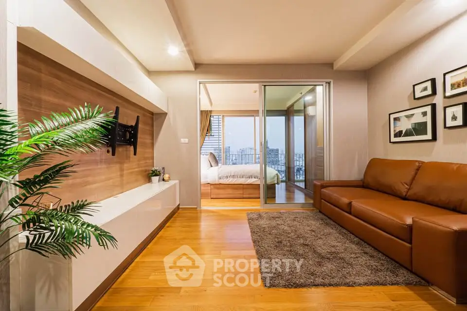 Modern living room with hardwood floors, leather sofa, and view into a cozy bedroom with cityscape.