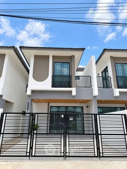 Modern two-story townhouse with sleek design and gated entrance under a clear blue sky.