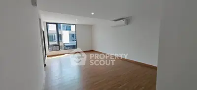 Spacious empty living room with wooden flooring and large window in modern apartment.
