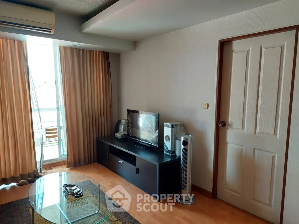 Cozy living room with balcony access, featuring modern entertainment setup and natural light.