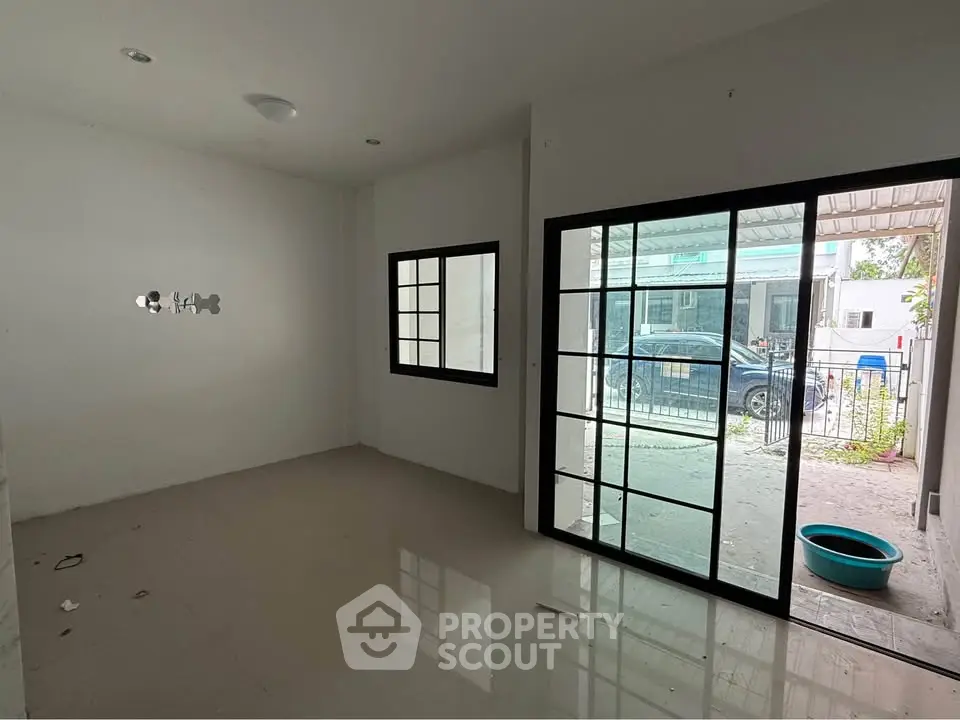 Spacious empty room with large windows and sliding glass door leading to outdoor area.