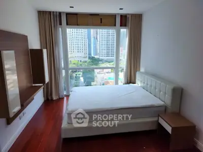 Spacious bedroom with large window offering city view and elegant wooden flooring.