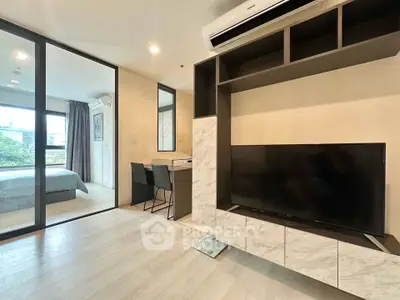 Modern apartment interior with open living area and bedroom, featuring sleek furniture and natural light.
