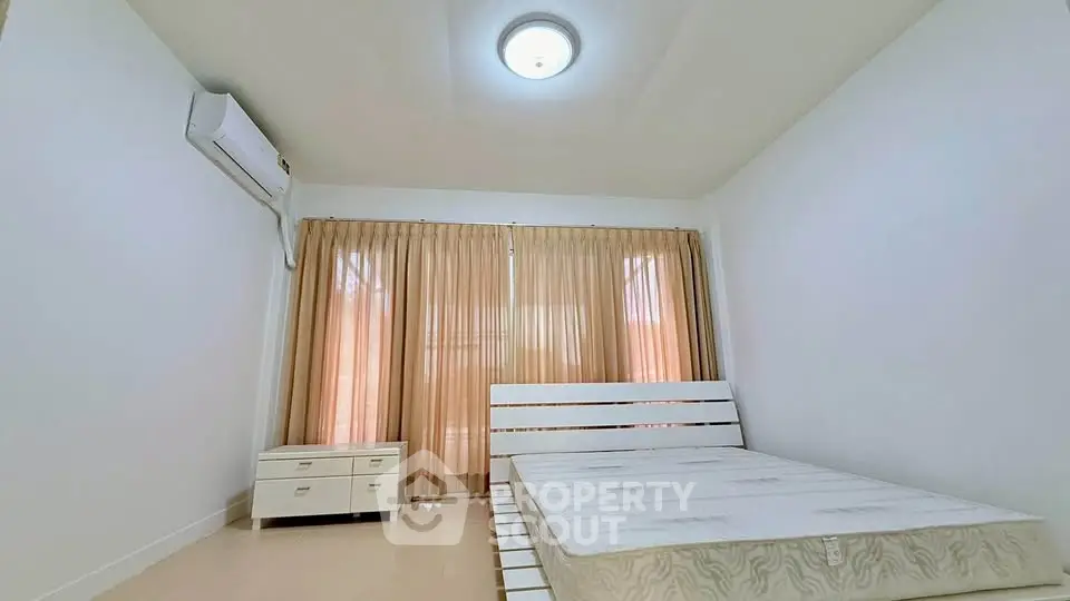 Spacious bedroom with natural light and minimalist decor, featuring a large window and air conditioning.