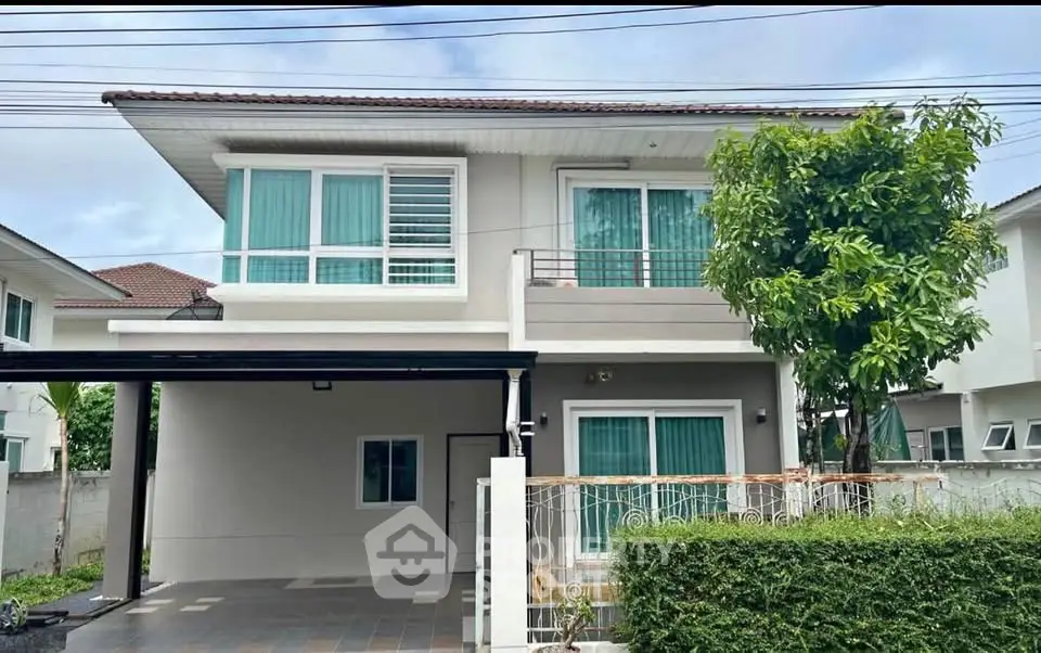 Modern two-story house with large windows and a carport, surrounded by greenery.