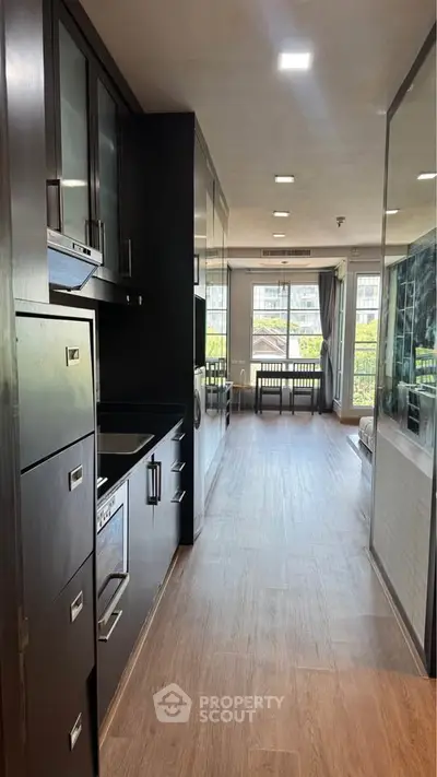 Modern kitchen with sleek cabinetry and open layout leading to a bright living area with large windows.