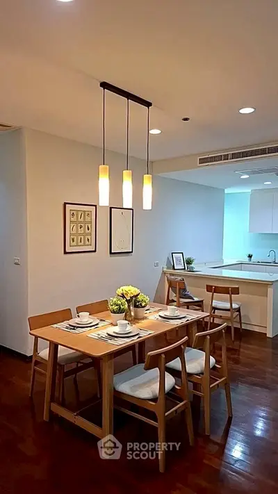 Modern dining area with elegant wooden table and chairs, adjacent to a sleek open kitchen layout.