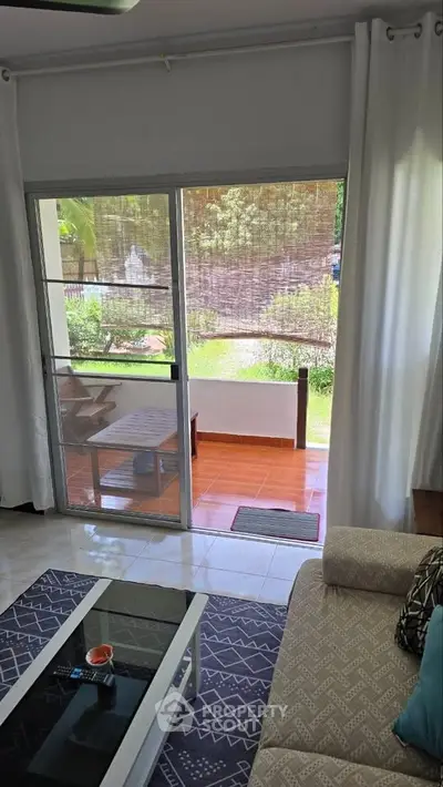 Charming living room with sliding glass doors opening to a cozy patio and lush garden view.