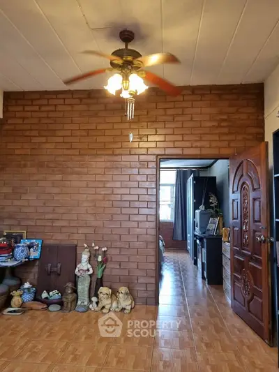 Charming living room with brick wall and ceiling fan, leading to a cozy bedroom.