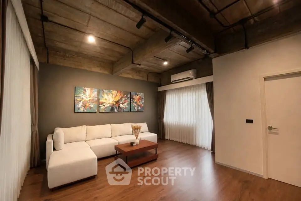 Modern living room with industrial ceiling and cozy white sofa, featuring stylish artwork and wooden flooring.