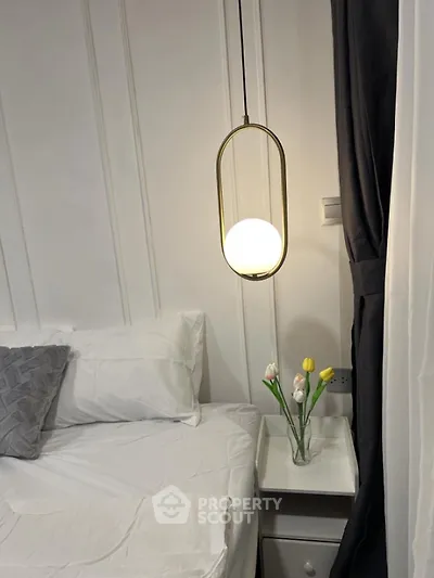 Cozy bedroom with modern pendant light and elegant white bedding, featuring a stylish nightstand with decorative flowers.