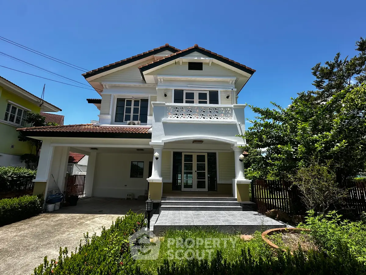Charming two-story house with lush garden and spacious driveway under clear blue sky.