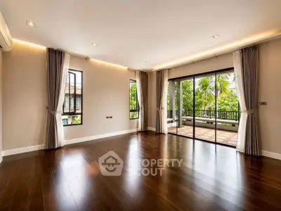 Spacious living room with hardwood floors and large windows opening to a lush balcony view.