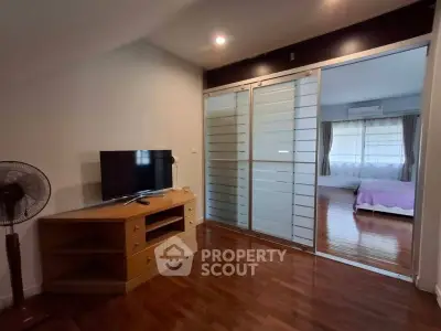 Spacious living room with wooden flooring and sliding glass doors leading to a cozy bedroom.