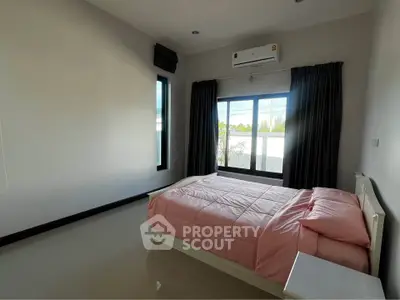 Spacious bedroom with large window and modern air conditioning unit, featuring a cozy bed with pink bedding.