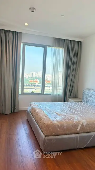 Spacious bedroom with large window offering stunning city views, featuring a comfortable bed and elegant curtains.